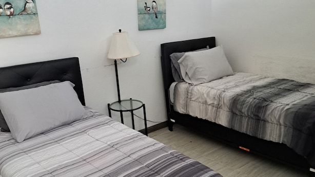 Ein Zimmer mit zwei Einzelbetten, einem kleinen runden Tisch, einer Stehlampe und zwei an der Wand hängenden Bildern.