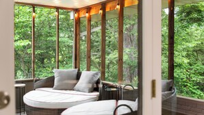 Ein Schlafzimmer mit einem großen Fenster mit Blick auf einen Wald. Es gibt zwei Betten mit weißer Bettwäsche und grauen Kissen.