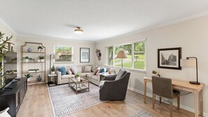 Ein Wohnzimmer mit einer Couch, Sesseln, einem Couchtisch, einem Schreibtisch und einem Bücherregal.