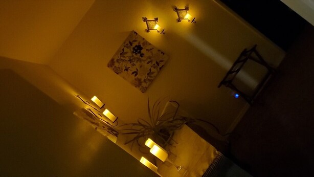 Una habitación con poca luz, una lámpara de mesa, una lámpara de pared y un cuadro en la pared.