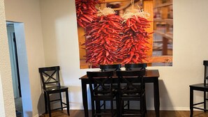 Un comedor con una mesa y sillas de madera, un cuadro grande de pimientos rojos en la pared y vistas a una zona de cocina.