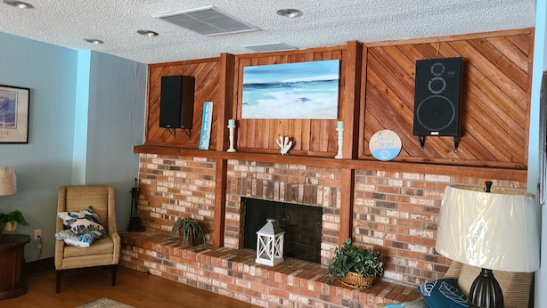A living room with a brick fireplace, a mounted TV, and a speaker.