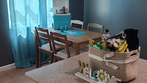 A dining area with a kitchen island, chairs, a table, a blue curtain, a painting, and a basket of snacks.