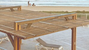 Une terrasse en bois avec des chaises longues et vue sur la plage.