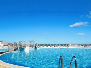 Ein klares, blaues Schwimmbecken mit einer Glasbrücke und Liegestühlen.