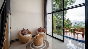 Ein modernes Interieur mit Rattanmöbeln, einem großen Fenster und Blick ins Grüne.