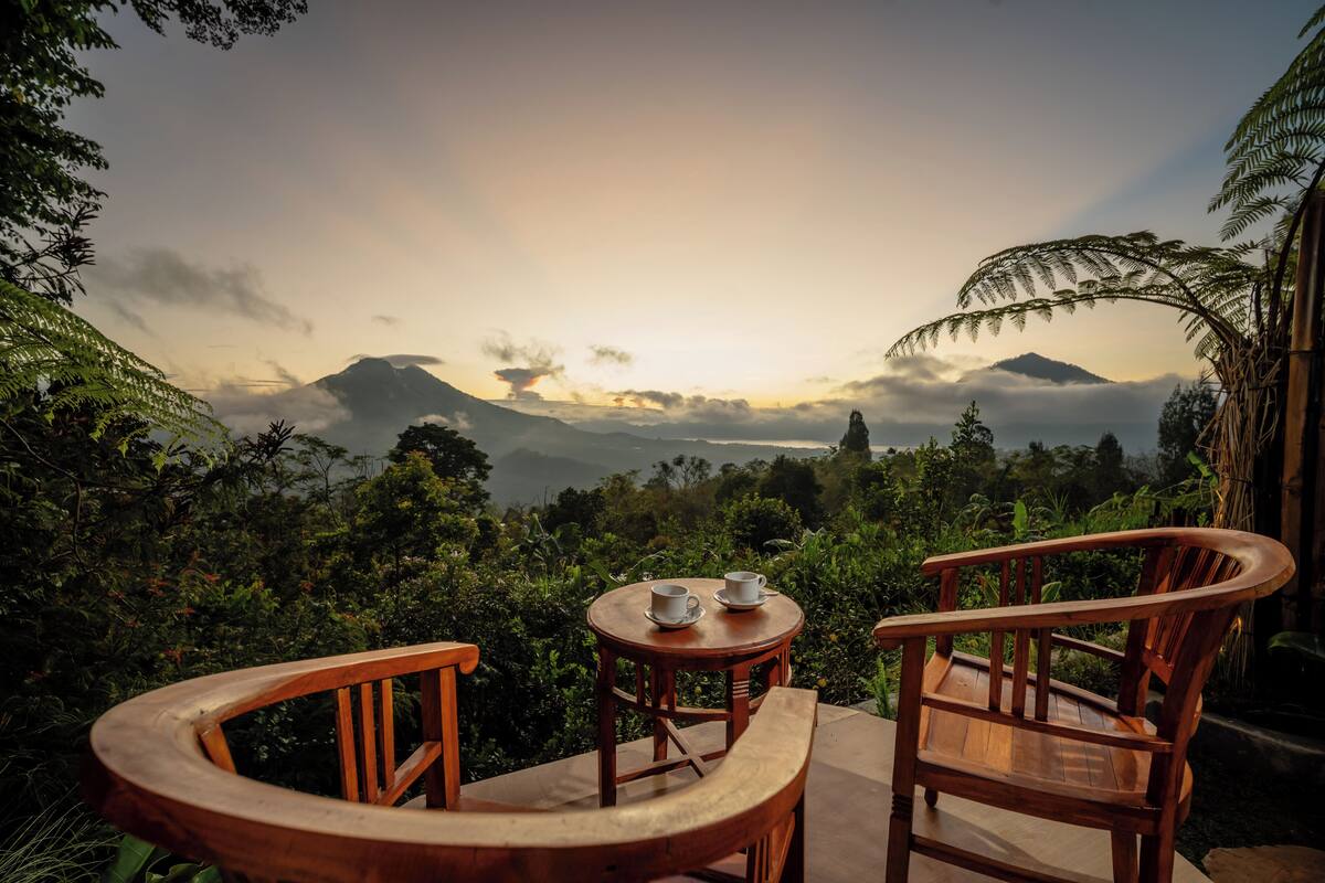A wooden table and chair set with two cups on a small table, overlooking a mountainous landscape with lush greenery.