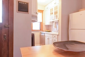 Une cuisine avec des meubles blancs, une table en bois et un panneau indiquant « BIENVENUE ».