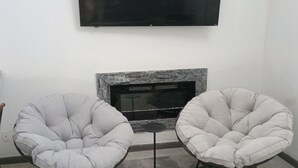 A living room with two armchairs, a fireplace, and a flat-screen TV mounted on the wall.