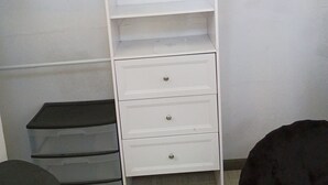 A white wardrobe with multiple shelves and drawers, a black trash bin, and a black ottoman.