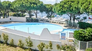 Ein Swimmingpool, umgeben von weißen Mauern und Bäumen, mit Blick auf Boote und einen Hafen im Hintergrund.