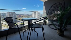 A balcony with two black wicker chairs and a small round table, overlooking a cityscape with high-rise buildings. - Apartamento Reñaca Live (Viña del Mar)