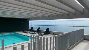 An indoor swimming pool with a view of the ocean, a covered area with lounge chairs, and a white fence. - Apartamento Reñaca Live (Viña del Mar)