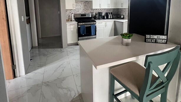 Una cocina moderna con armarios blancos, una isla grande y un área de comedor con una silla.