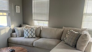 Una sala de estar moderna con un sofá seccional color beige, una mesa de centro redonda de madera y un piso de baldosas de mármol.