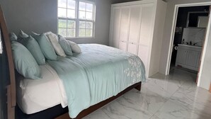 Un dormitorio con cama, ventana, unidad de aire acondicionado, armario y baño visible a través de una puerta abierta.