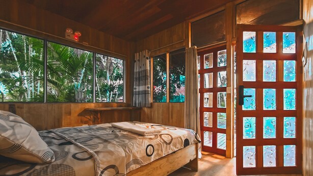 Une pièce en bois avec un lit, une fenêtre et une porte dont les panneaux sont en verre dépoli.