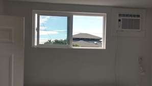 A bedroom with a bed, two pillows, a window, and an air conditioning unit.