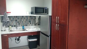 A compact kitchen with a microwave, refrigerator, and tiled backsplash.
