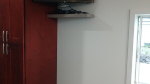 A room with a wooden wardrobe, a mounted television, and a window.