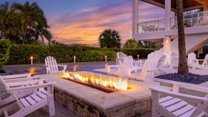 Zona junto a la piscina con sillas Adirondack blancas, una chimenea y un edificio moderno con balcón.