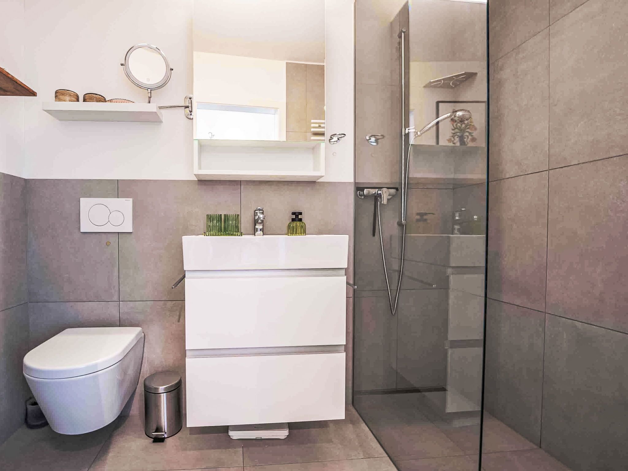 Une salle de bain moderne comprenant des toilettes, un bidet, un meuble-lavabo avec un miroir et une douche à parois de verre.