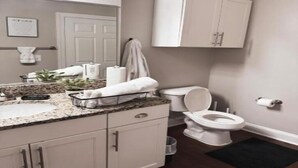 Une salle de bain avec un lavabo blanc, un plan de toilette et des meubles de rangement blancs, des toilettes et un porte-serviettes.