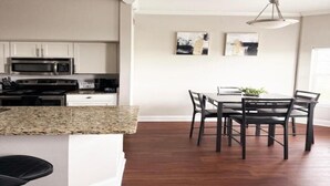 Une cuisine moderne avec des meubles blancs, un plan de travail en granit et un coin repas comprenant une table et des chaises.