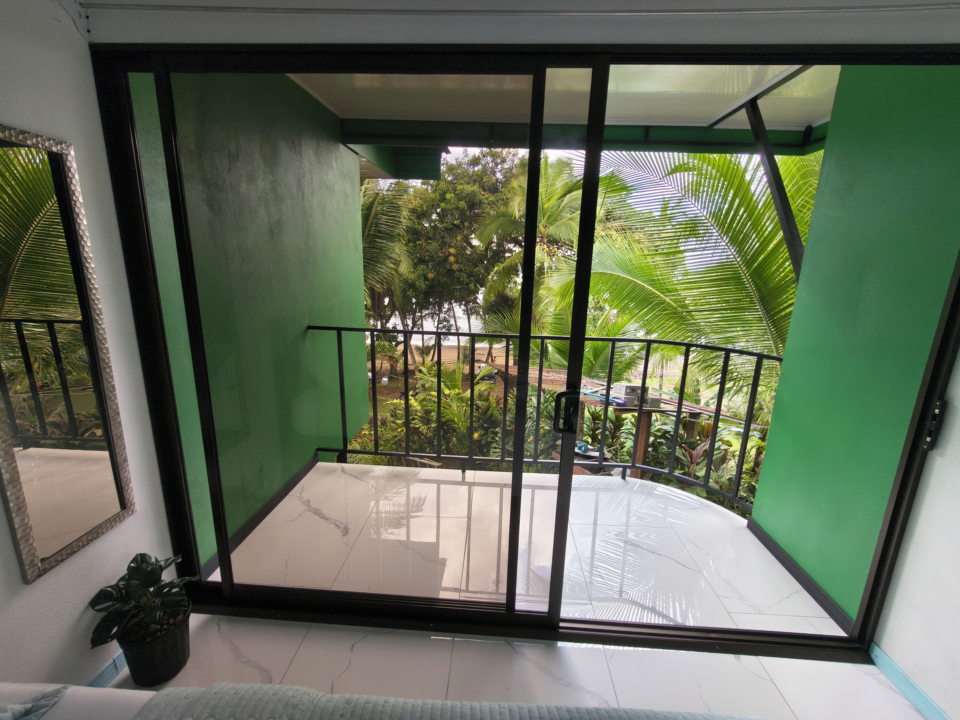 A balcony with a view of a garden, a tiled floor, and a black railing.
