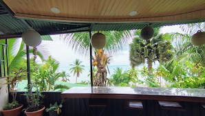 Un bar extérieur abrité, avec vue sur l’océan et les palmiers.