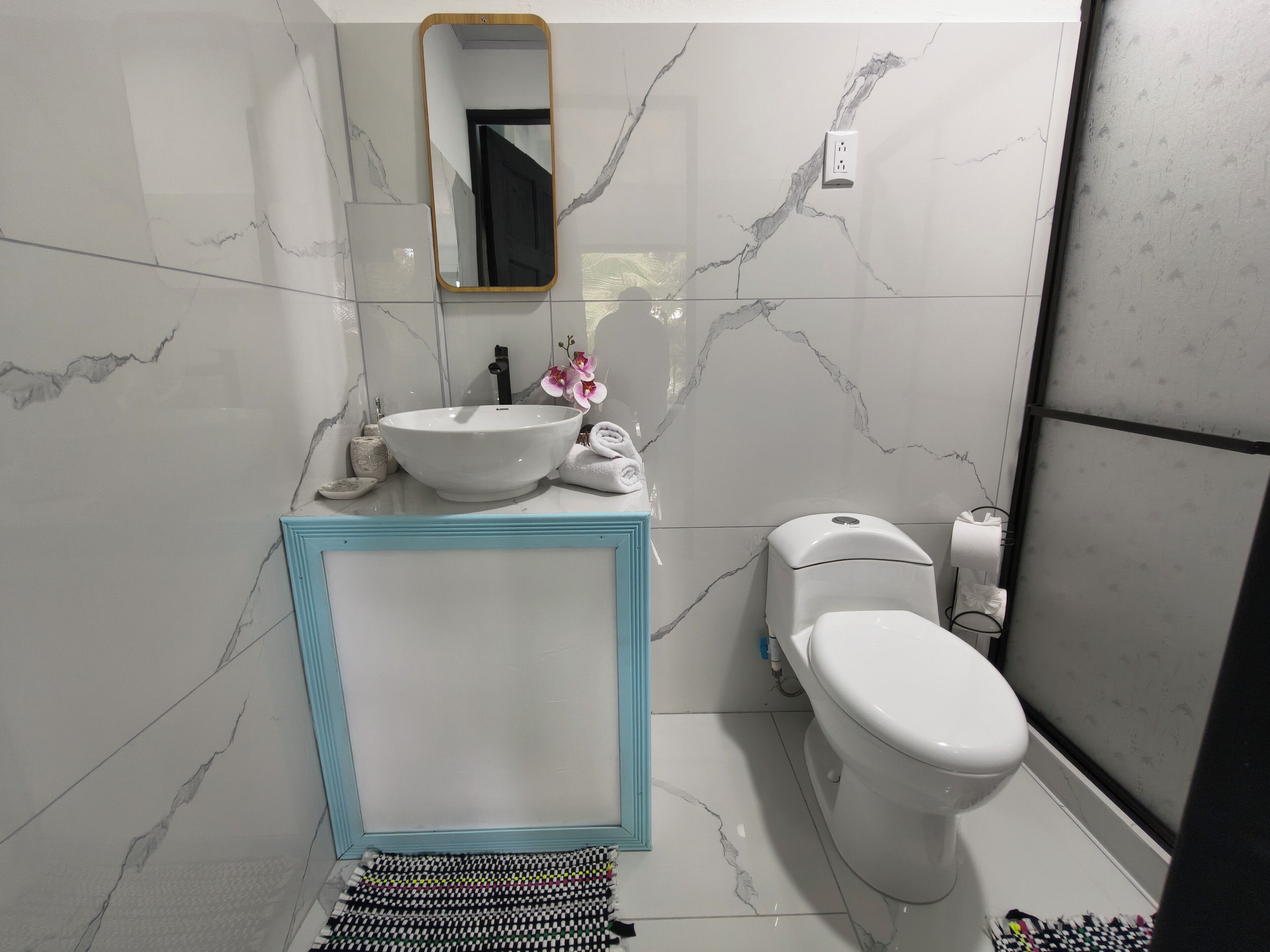 Een badkamer met een marmeren spatwand, een wastafel met een blauwe omlijsting, een toilet en een spiegel.