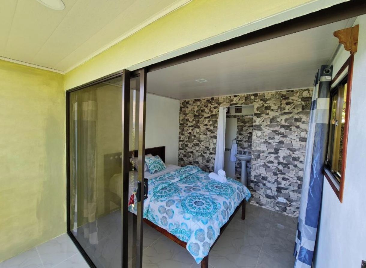 A bedroom with a bed, a bedside table, a wall with a stone pattern, and a sliding glass door leading to another room.