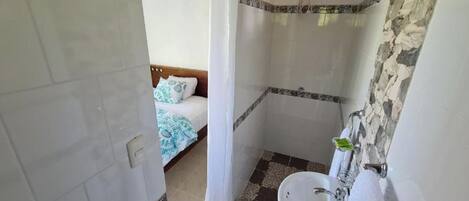 Une salle de bain avec une douche, un lavabo et un lit recouvert d’une courtepointe bleue et blanche.