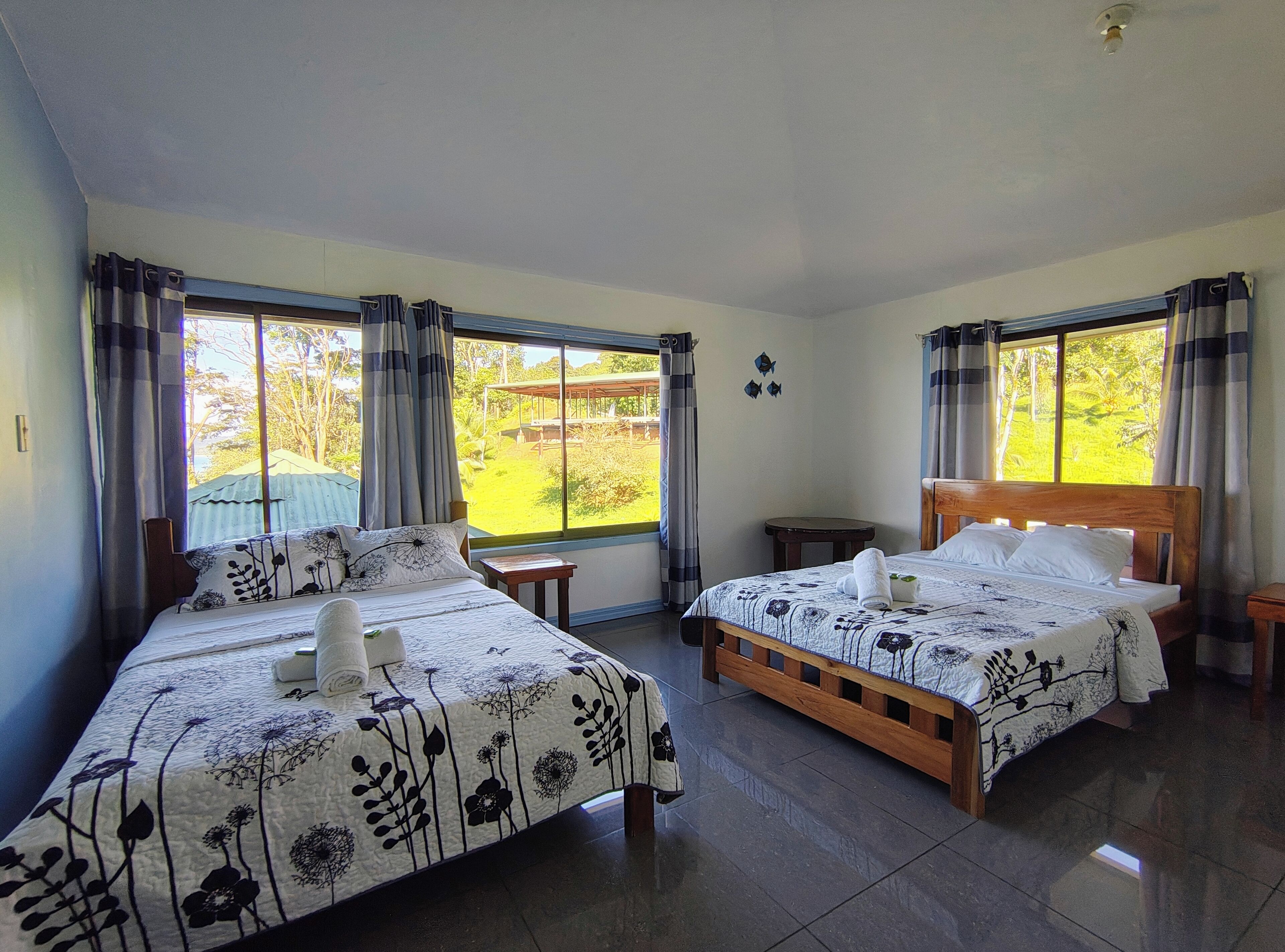 A hotel room with two beds, large windows, a small table, and a ceiling light.