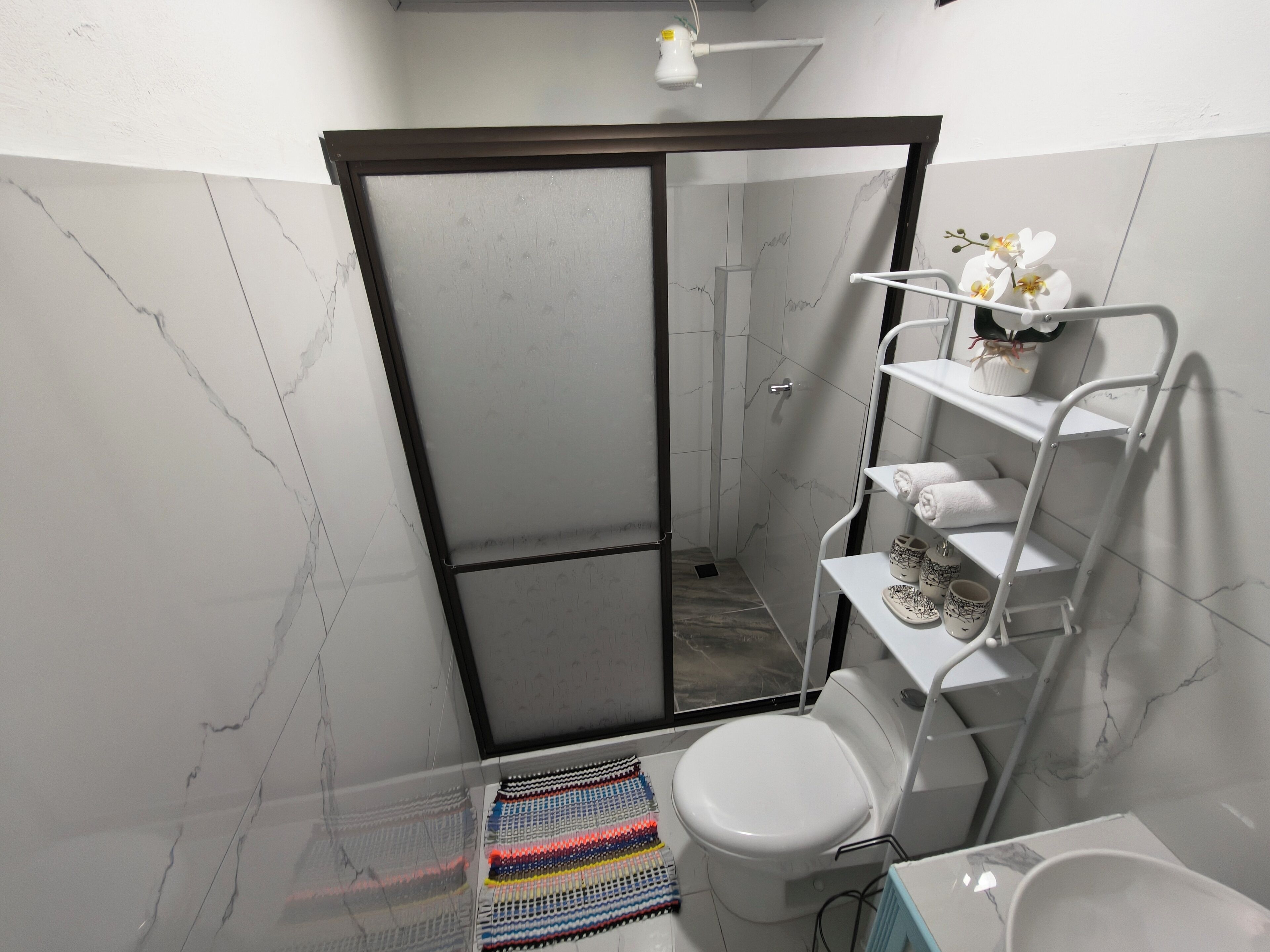 A bathroom with a shower, toilet, and white shelves with towels and a potted plant.