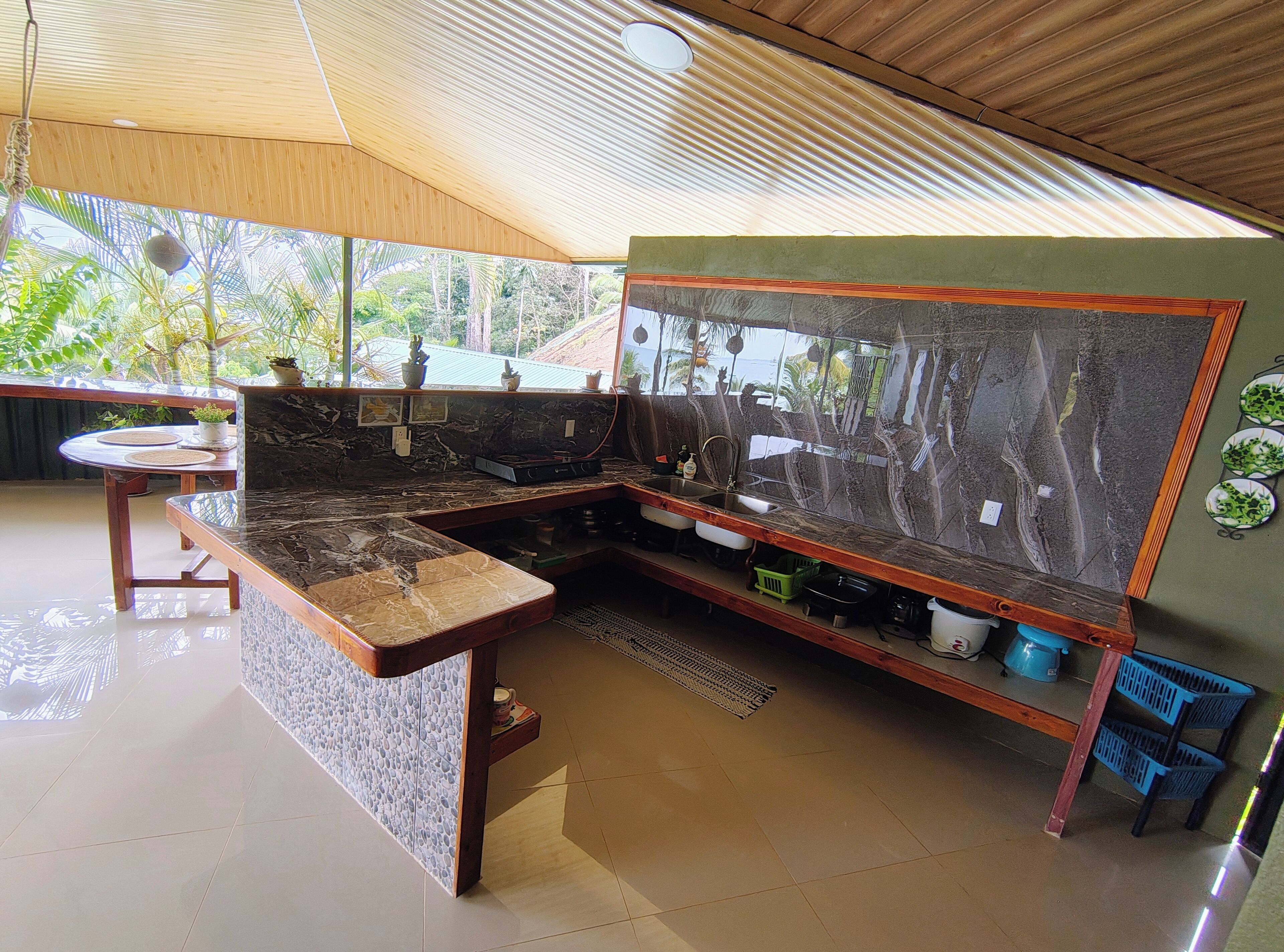 A modern kitchen with a marble countertop, wooden cabinets, and a large window overlooking greenery.