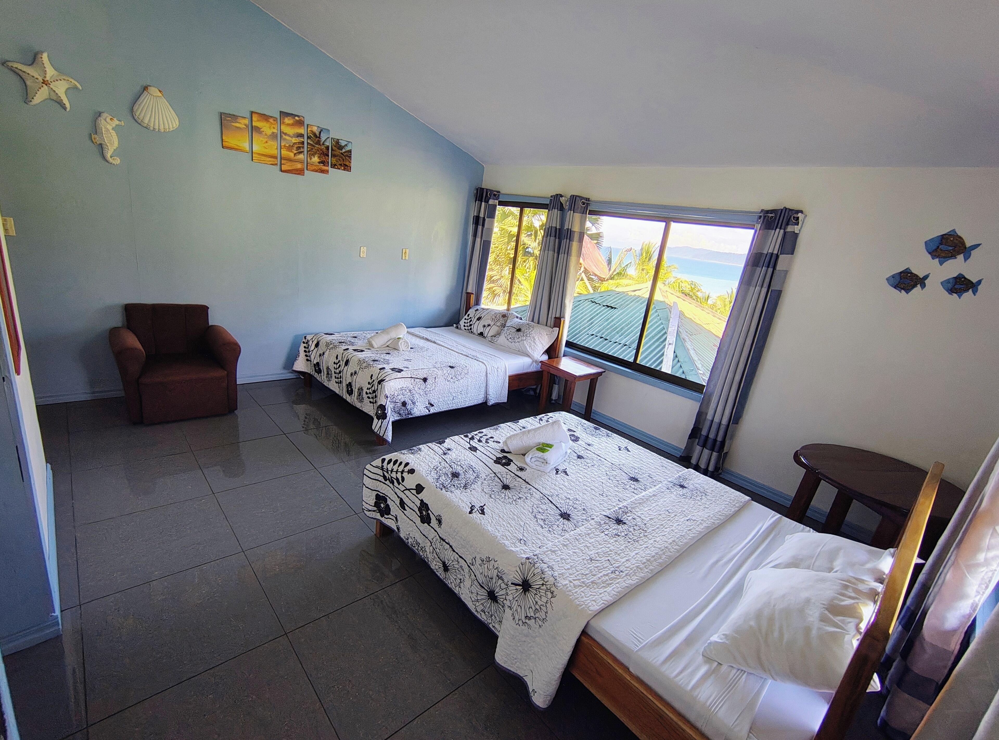 Une chambre avec deux lits, une chaise et une vue sur la mer.