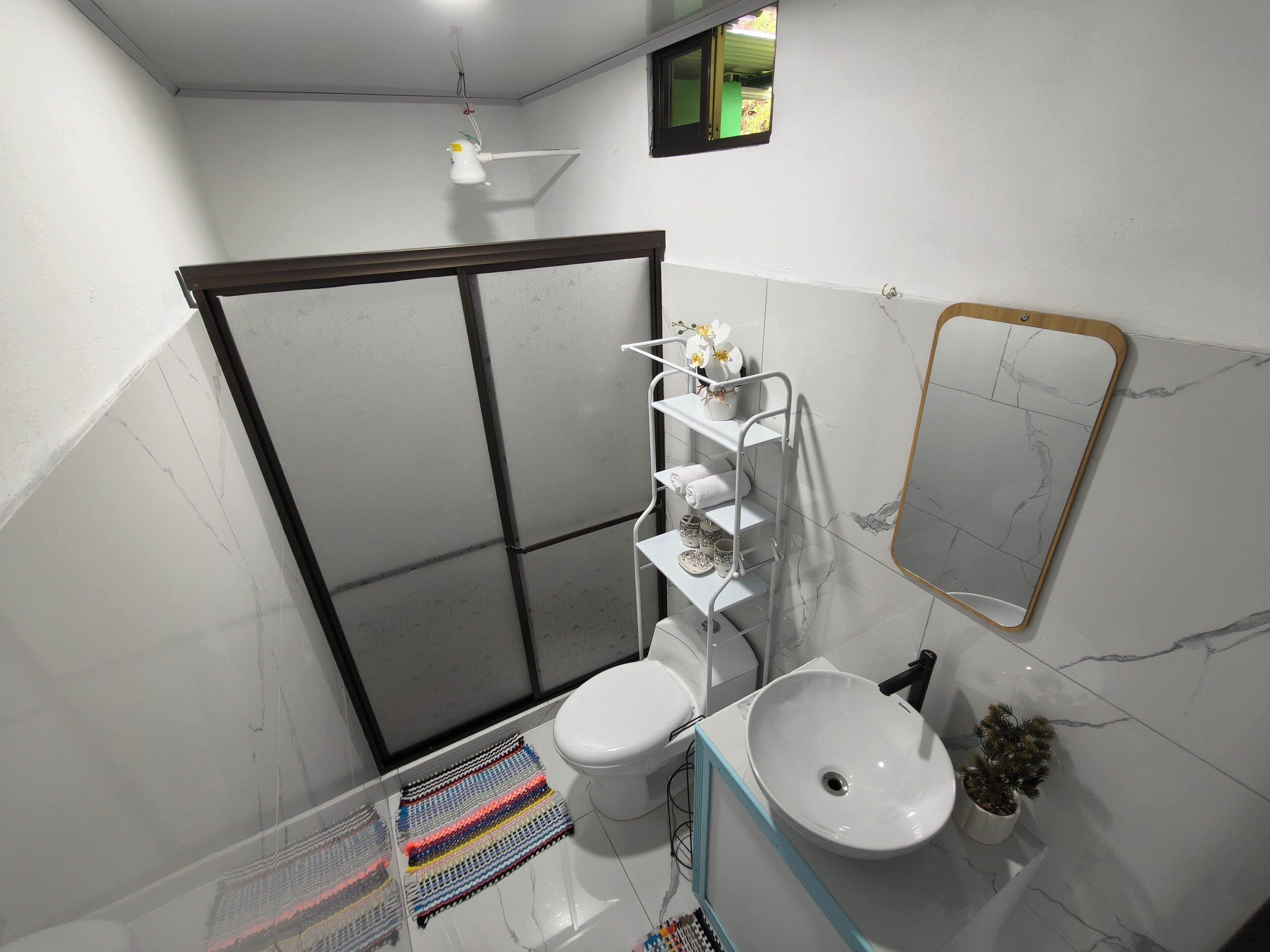 A bathroom with a shower, toilet, sink, and a mirror.
