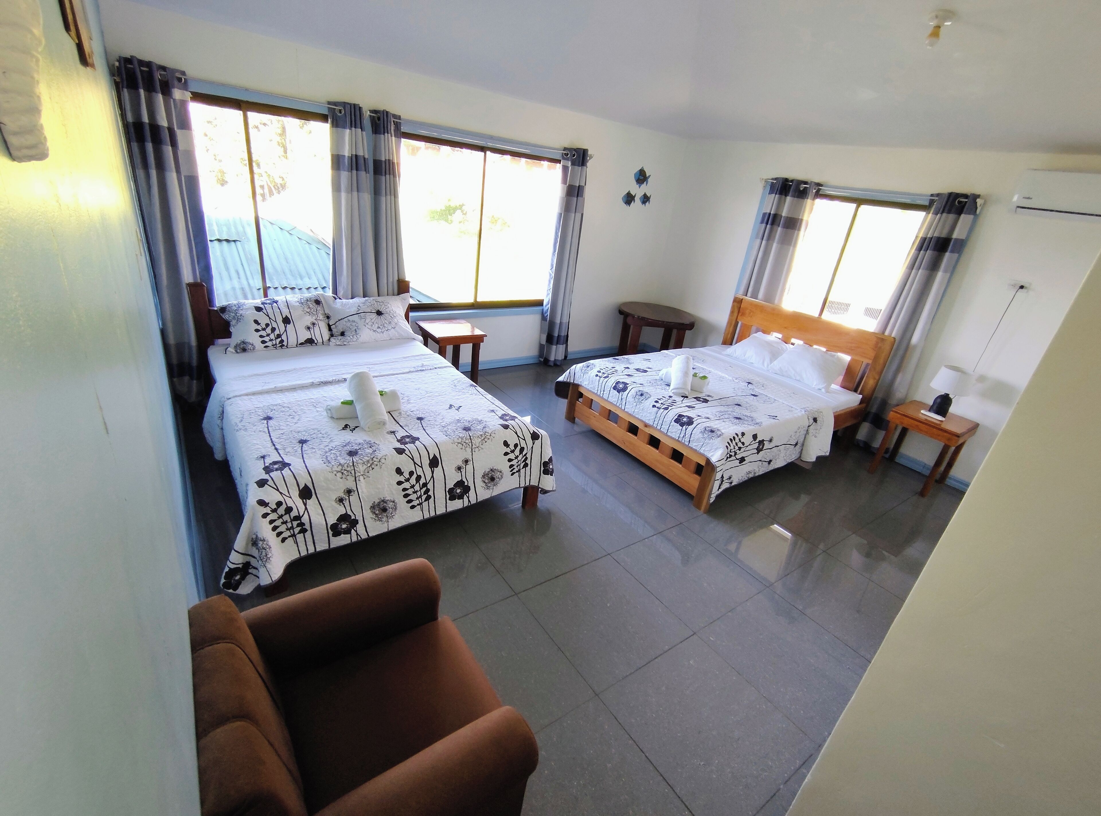 A hotel room with two beds, a wooden headboard, a small table, a chair, and a view of the outside.