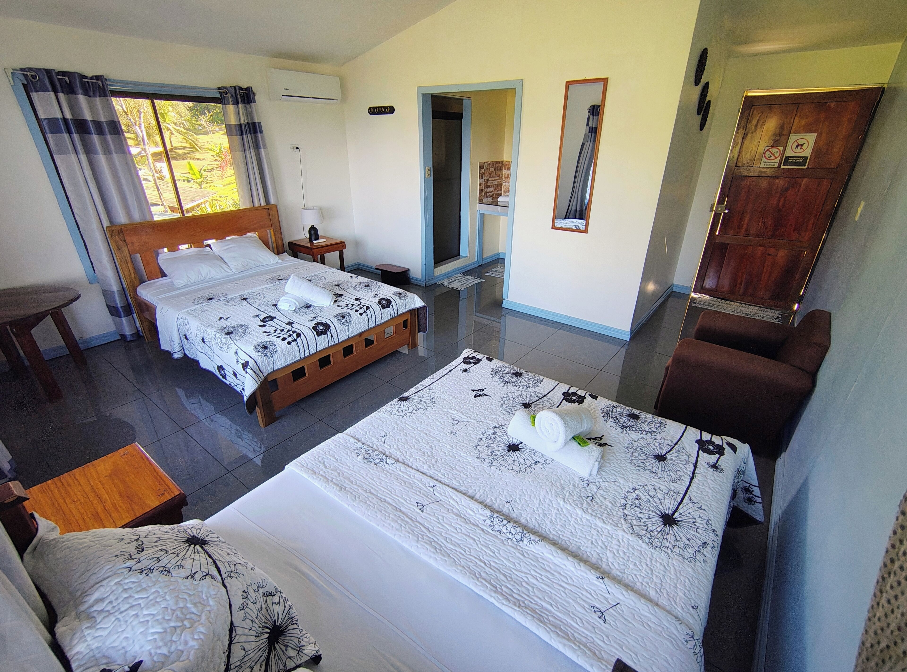 A hotel room with two beds, a wooden headboard, a small table, a chair, and a wardrobe.