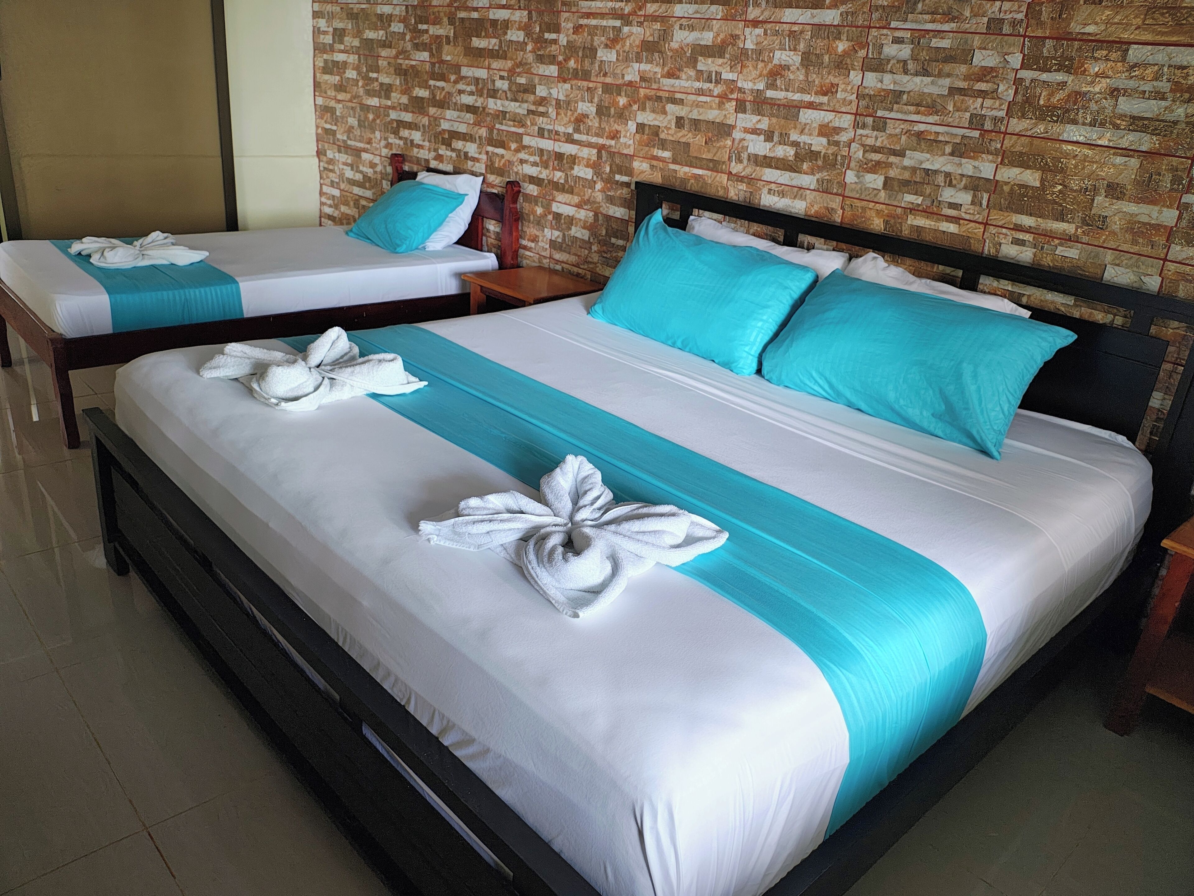 Two twin beds with white and turquoise bedding, a wooden headboard, and a brick-patterned wall.