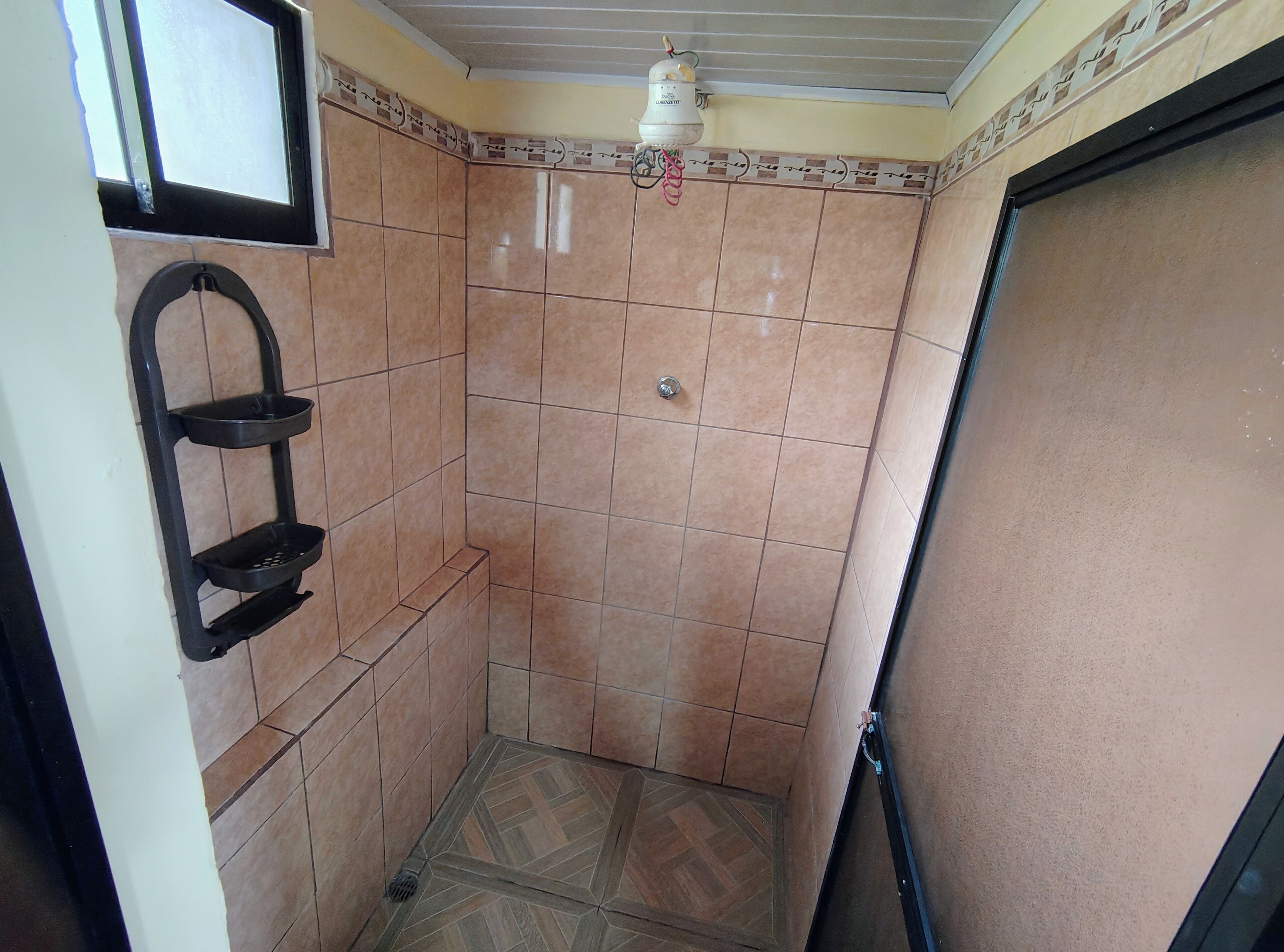Un baño pequeño con azulejos, ducha, inodoro y lavamanos.