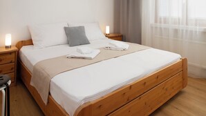 A neatly made bed with white linens, a grey pillow, and a wooden headboard. There are two bedside tables with lamps, and a window with sheer curtains. - La Siala Apt.19 by Interhome (Falera)
