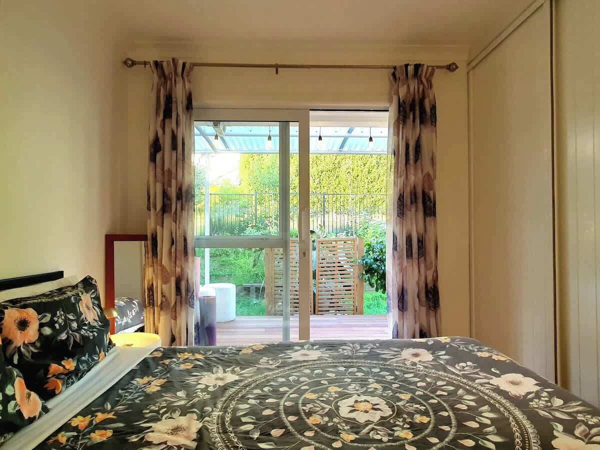 A bedroom with a bed, curtains, and a view of an outdoor deck.