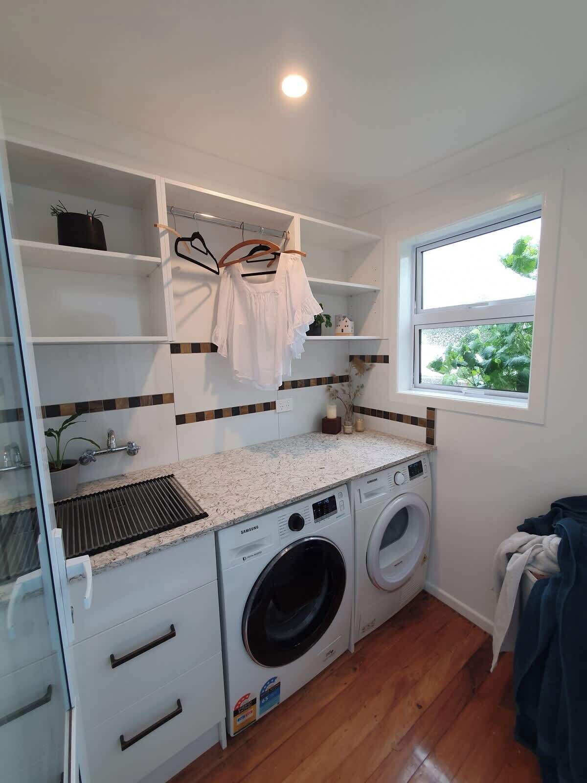 A compact laundry room with a washing machine, drying rack, and shelving.