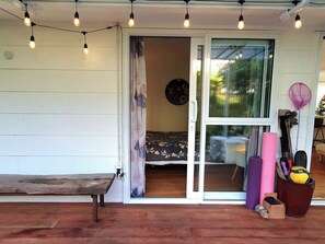 A wooden bench outside a room with a sliding glass door, a string of lights, and a yoga mat. - Garden View, Sherwood Forest - Tauranga (Tauranga)