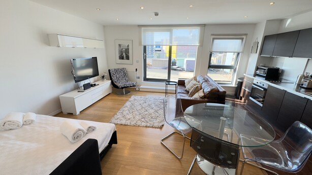 A modern living room with a sofa, a glass dining table, a TV, and a kitchen area with a stove and oven. - 2-bed Apt, Sleeps 7, 5 Mins to Camden Market (London)