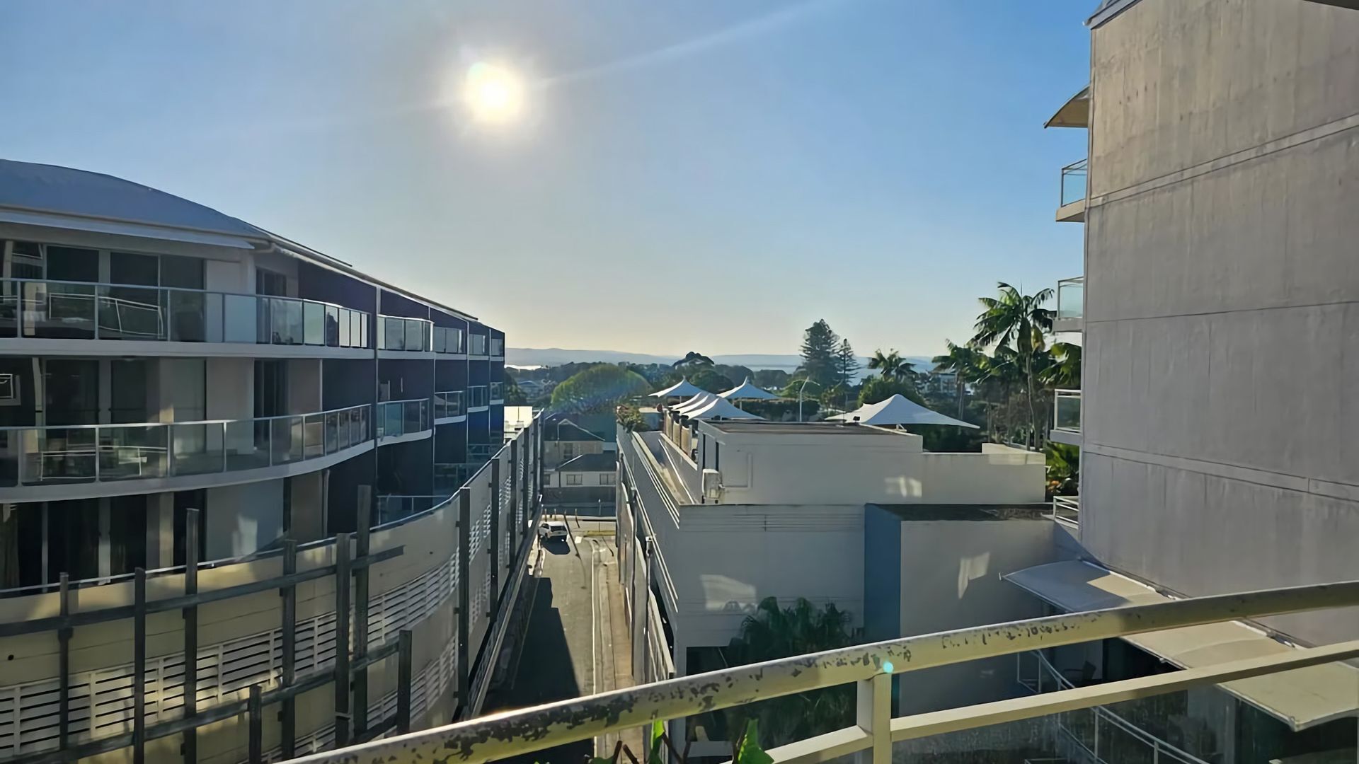 A multi-story building with balconies, a clear sky, and distant mountains.