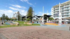Un parc public doté d’aires de jeux, d’espaces pour s’asseoir et d’un bâtiment moderne avec des balcons.