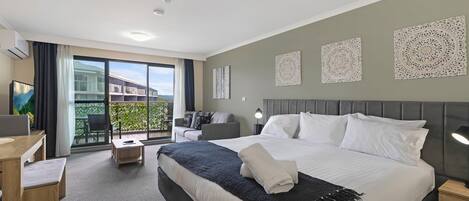 Ein Hotelzimmer mit einem großen Bett, einem Schreibtisch, einem Stuhl und einem Balkon mit Blick.